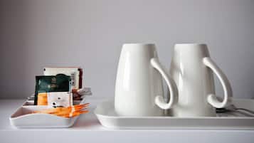 Two white ceramic mugs on a white tray, a white plate with some food items, and a few packets of tea.