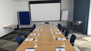 Una sala de conferencias con una larga mesa, sillas, una pantalla de proyector y una pizarra.