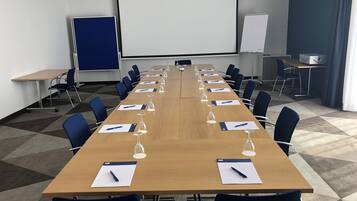 Ein Konferenzraum mit langem Tisch, Stühlen, einer Projektionsleinwand und einer Whiteboard-Tafel.