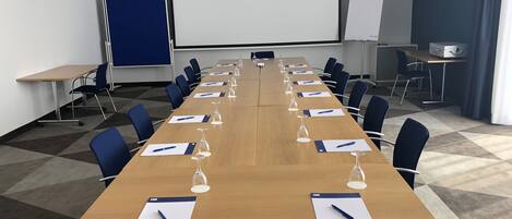 Una sala de conferencias con una larga mesa, sillas, una pantalla de proyector y una pizarra.