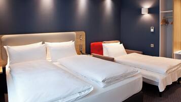 Ein Hotelzimmer mit zwei Betten, einem hölzernen Kopfteil, einem roten Sessel und einem kleinen Tisch mit einer Lampe.