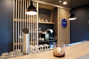 Zona de bar con una máquina de café, estantes con botellas y un cartel que dice 