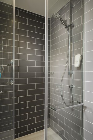 A modern shower with a glass door, a handheld showerhead, and a wall-mounted control panel.