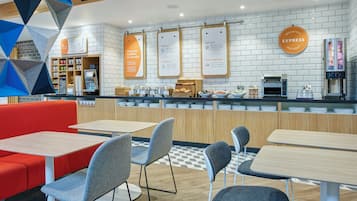 A modern cafe with a breakfast bar, seating area, and a variety of food and drink options.