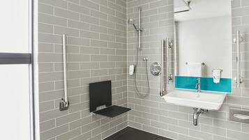 Un bagno moderno con pareti rivestite in piastrelle grigie, uno scaffale nero, un lavandino bianco con un dettaglio blu e un soffione doccia a mano.