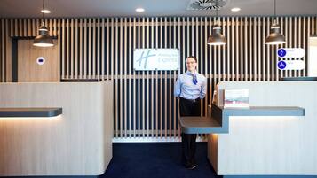 L'espace d'accueil d'un hôtel Holiday Inn Express, doté d'un design moderne, avec un mur en panneaux de bois verticaux, un comptoir d'accueil et un éclairage suspendu.