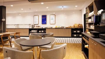 A modern cafe interior with round tables, chairs, and a counter with food items.