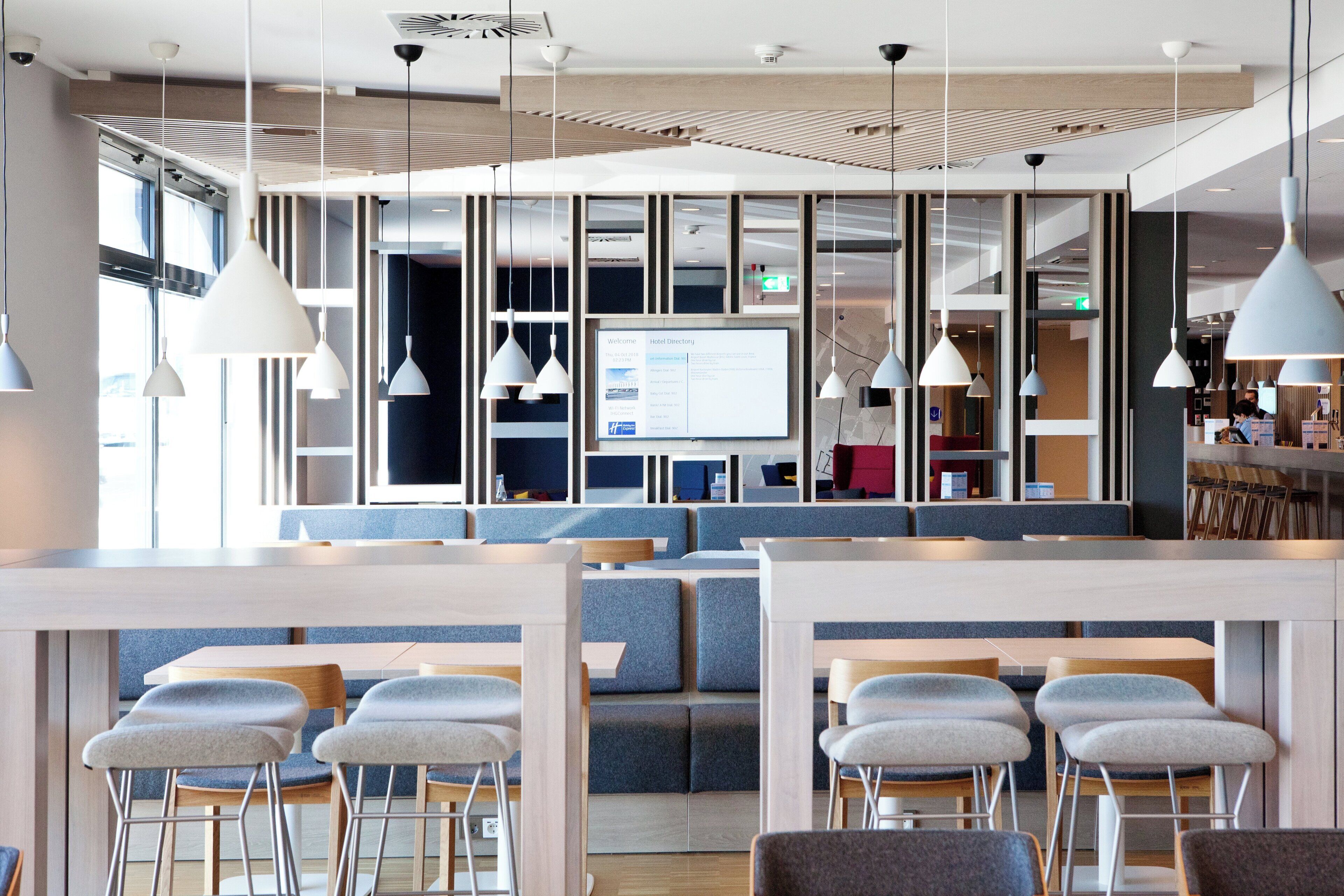 Un moderno vestíbulo de hotel con zonas de estar, un mostrador de recepción y una pantalla digital.