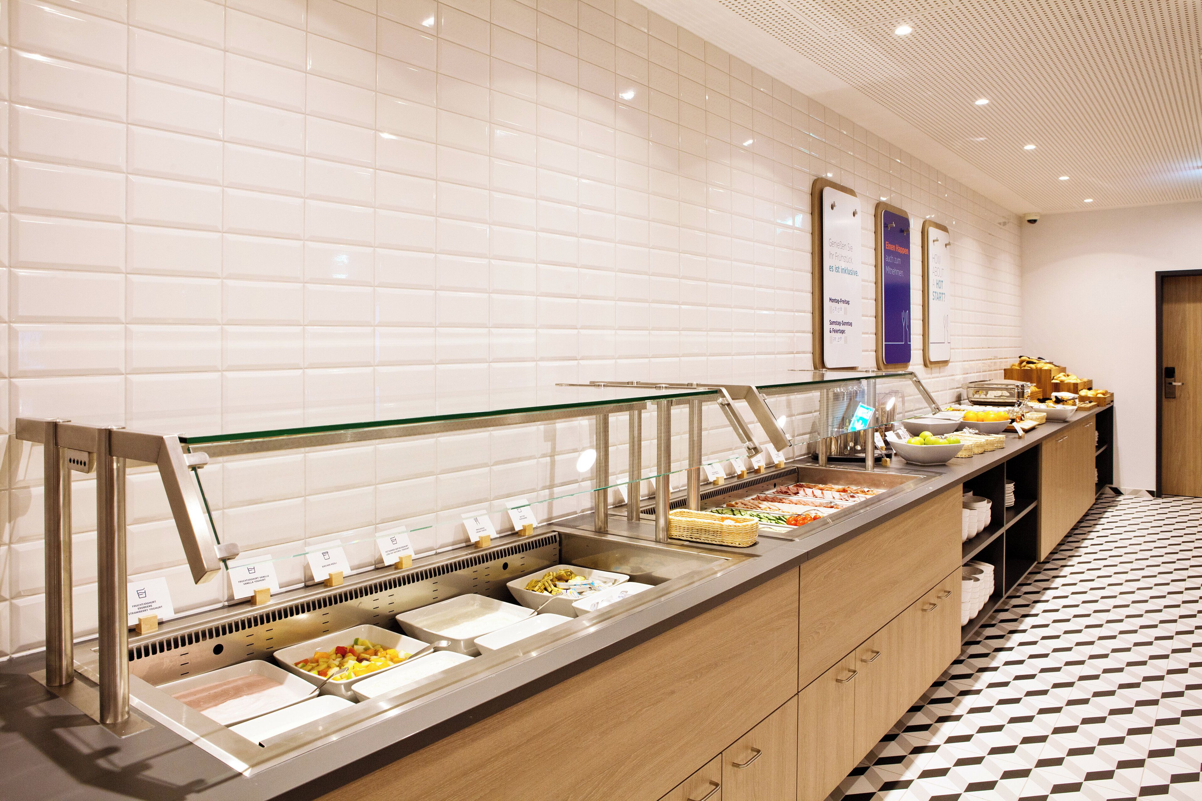 A buffet area with various food options, a tiled wall, and a patterned floor.
