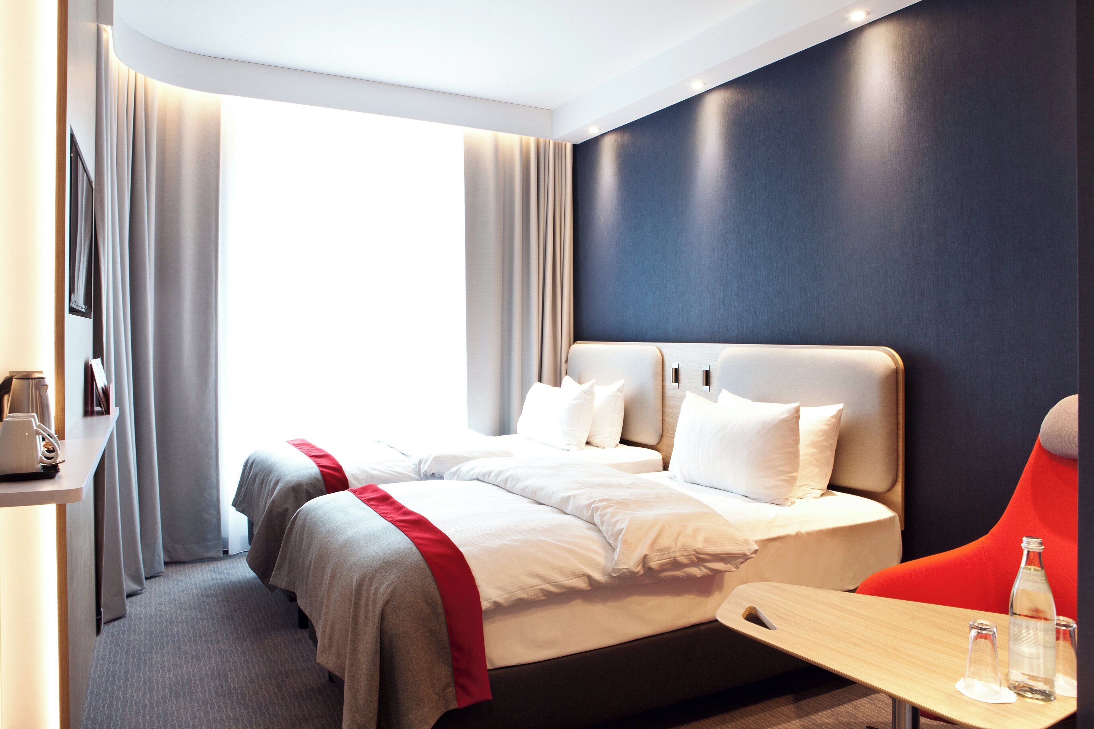 A hotel room with a bed, bedside tables, a desk, and a view of the outdoors.