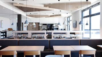 Un restaurante moderno con techos altos, iluminación colgante y una zona de bar al fondo.