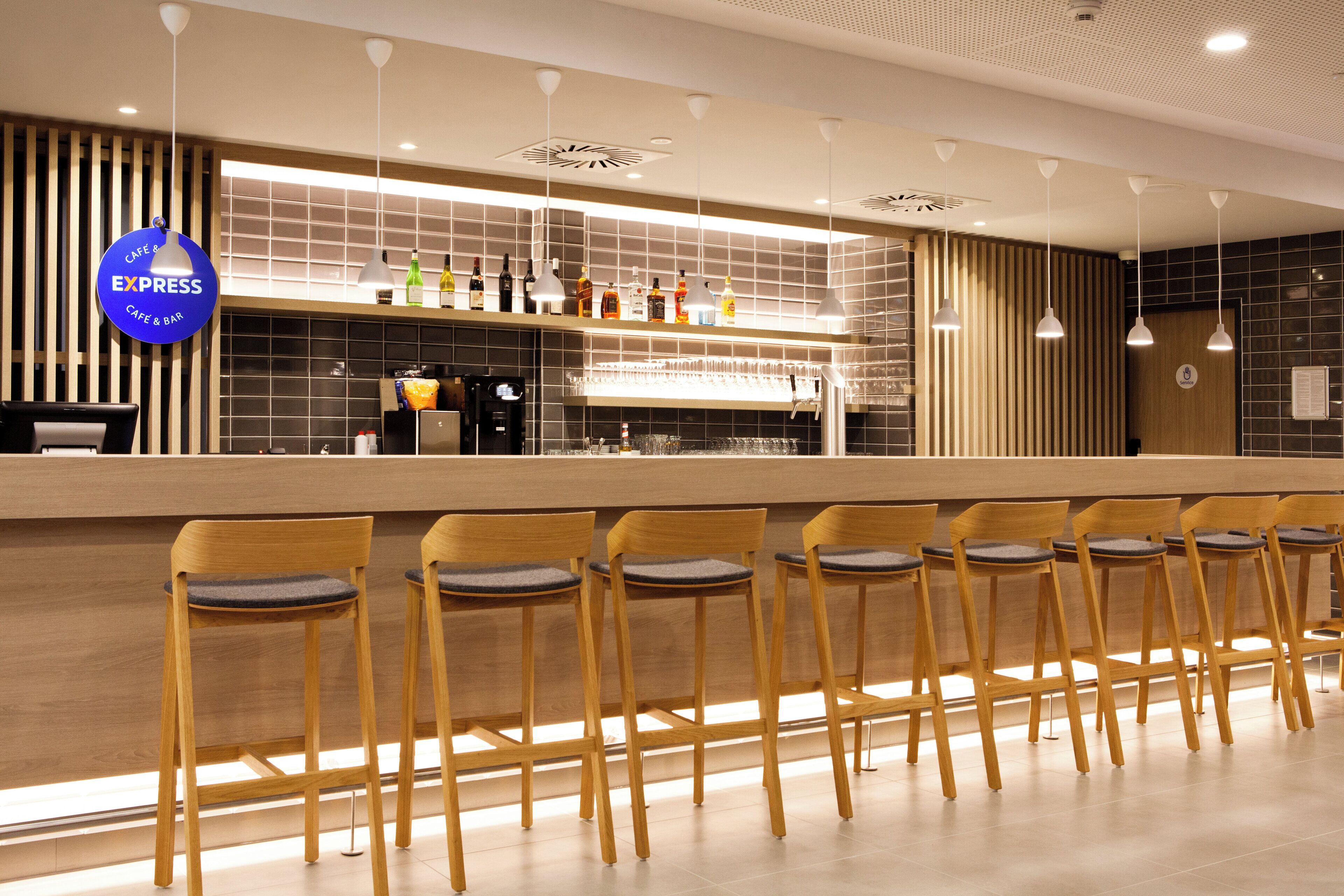 Un área de bar moderna con una barra larga, varios taburetes y una variedad de botellas en la estantería.