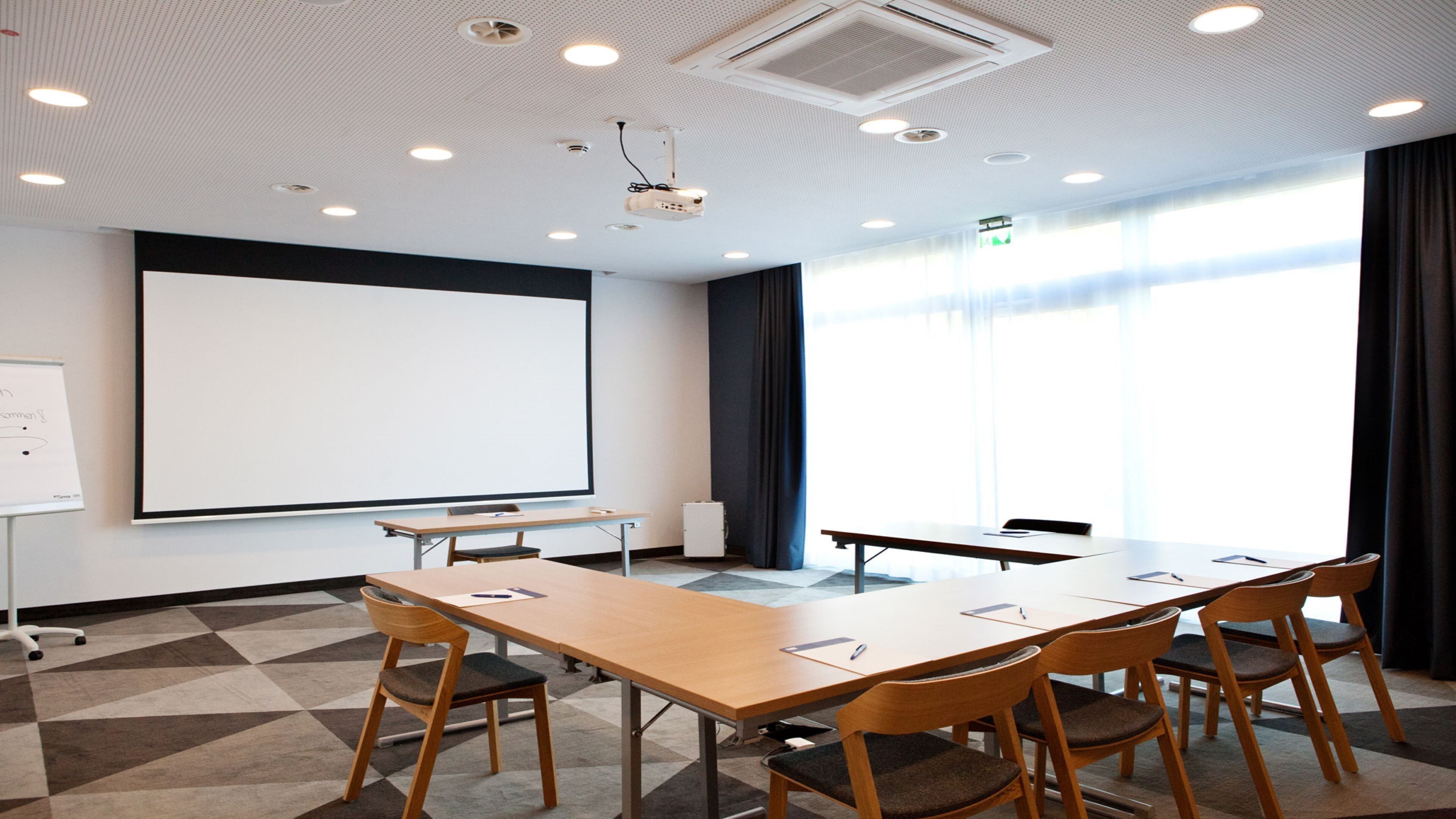 A conference room with a large whiteboard, a projector, a long table with chairs, and a large window with curtains.
