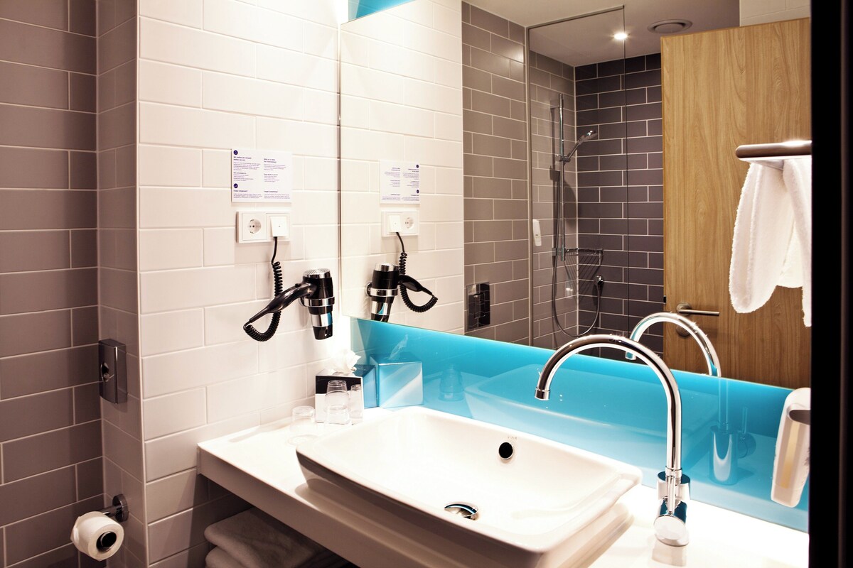 A modern bathroom with a white sink, a blue countertop, a glass shower enclosure, and a wooden door.