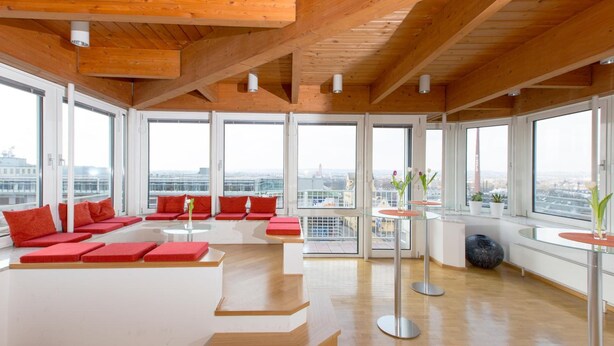 Una habitación amplia con ventanas grandes, vigas de madera en el techo y asientos acolchados rojos.