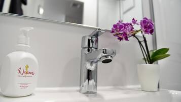 Ein Badezimmer mit einem chromfarbenen Wasserhahn, einer weißen Shampooflasche und einer Topf-Orchidee.