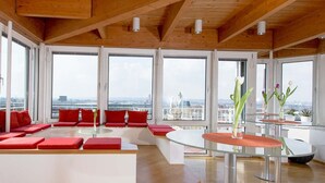 Un amplio salón con asientos rojos, ventanas grandes y vistas a la ciudad.