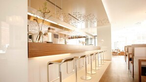 Un área de bar moderna con una barra larga, varios taburetes y una cocina visible al fondo.