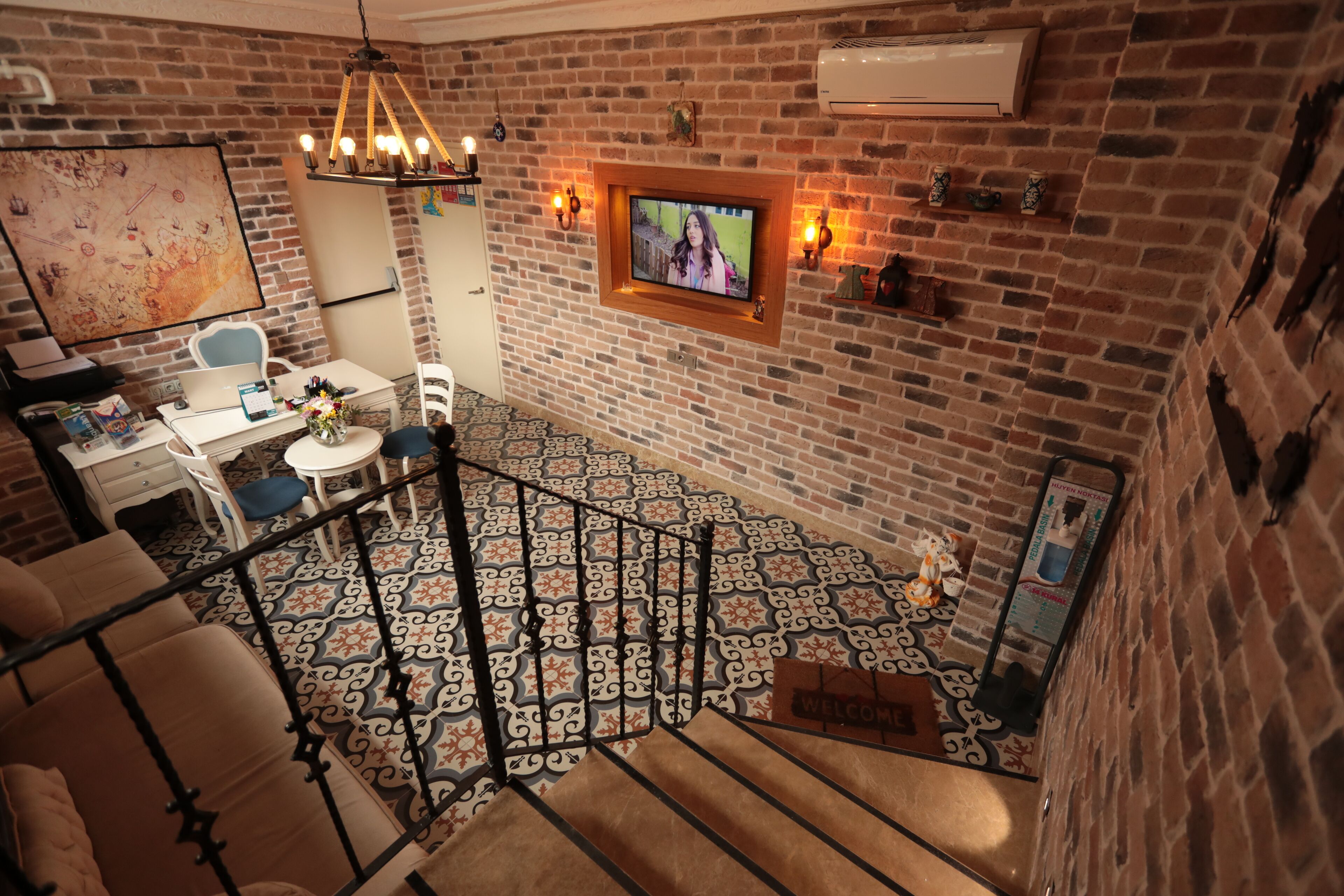 Une pièce avec un mur en briques, un téléviseur fixé au mur, un bureau avec une chaise, une petite table avec un vase et un sol à motifs.