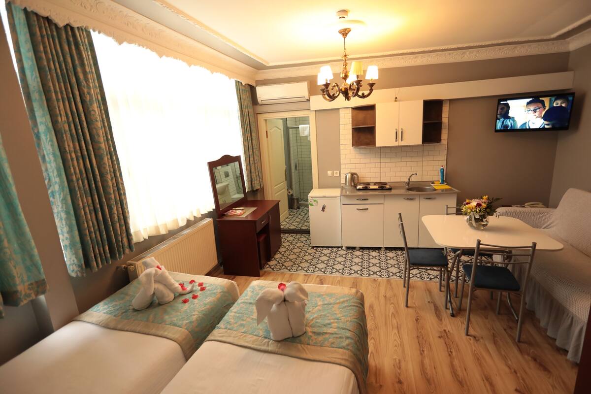 A hotel room with two beds, a kitchenette, a dining area, and a TV.