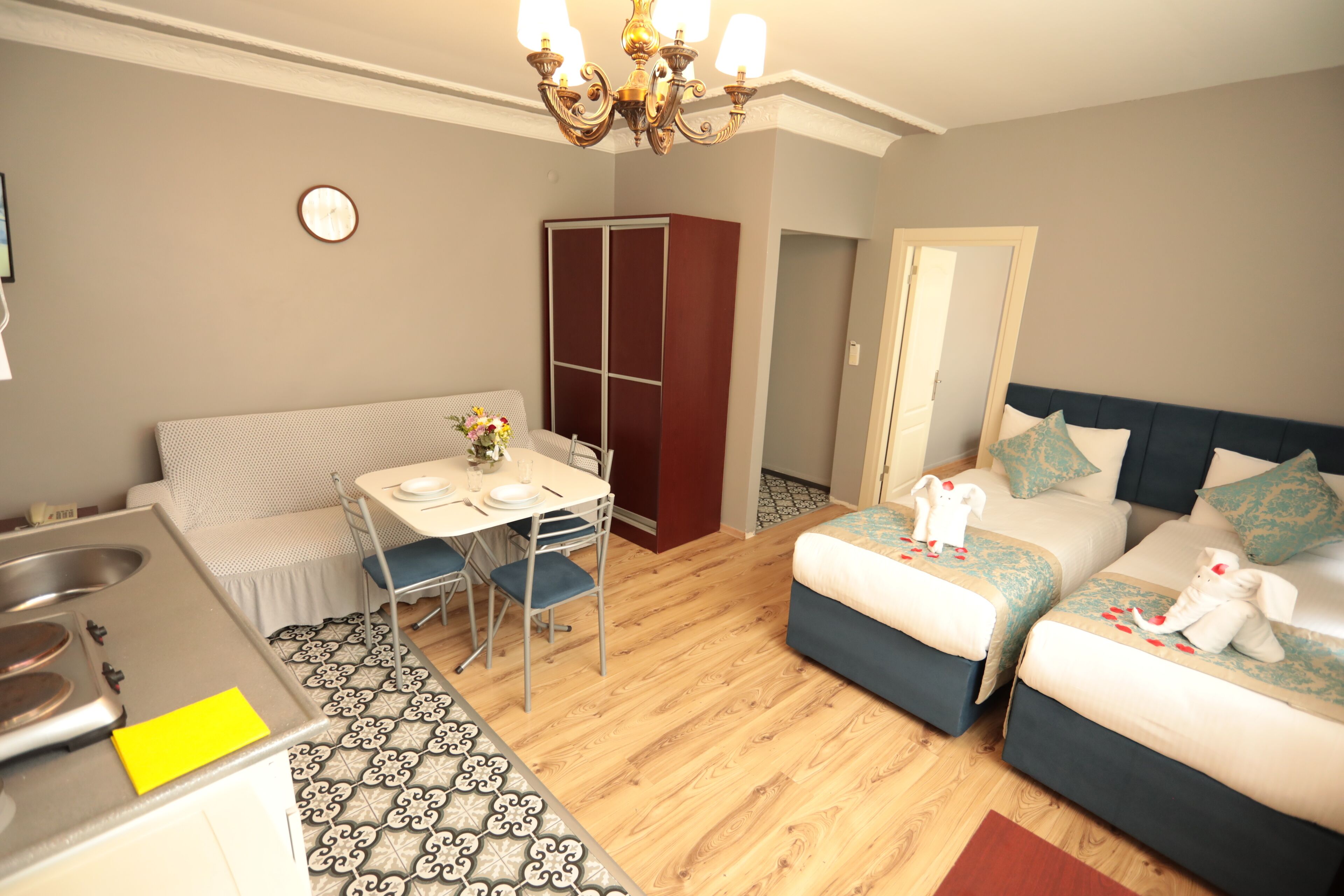 Una habitación de hotel compacta con kitchenette, dos camas, zona de comedor y armario.
