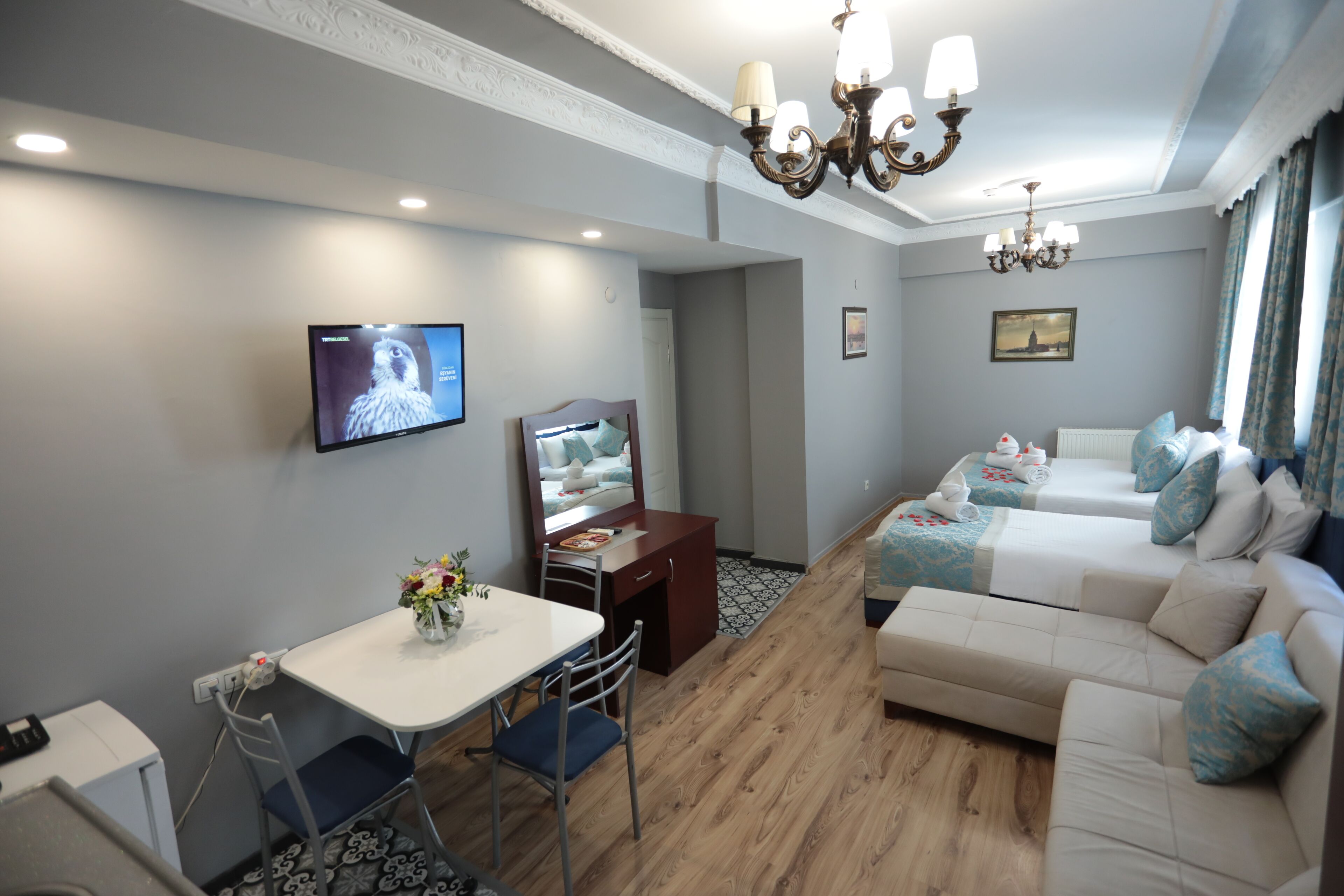 Quarto de hotel com área de refeições, televisão, cama e lustre.