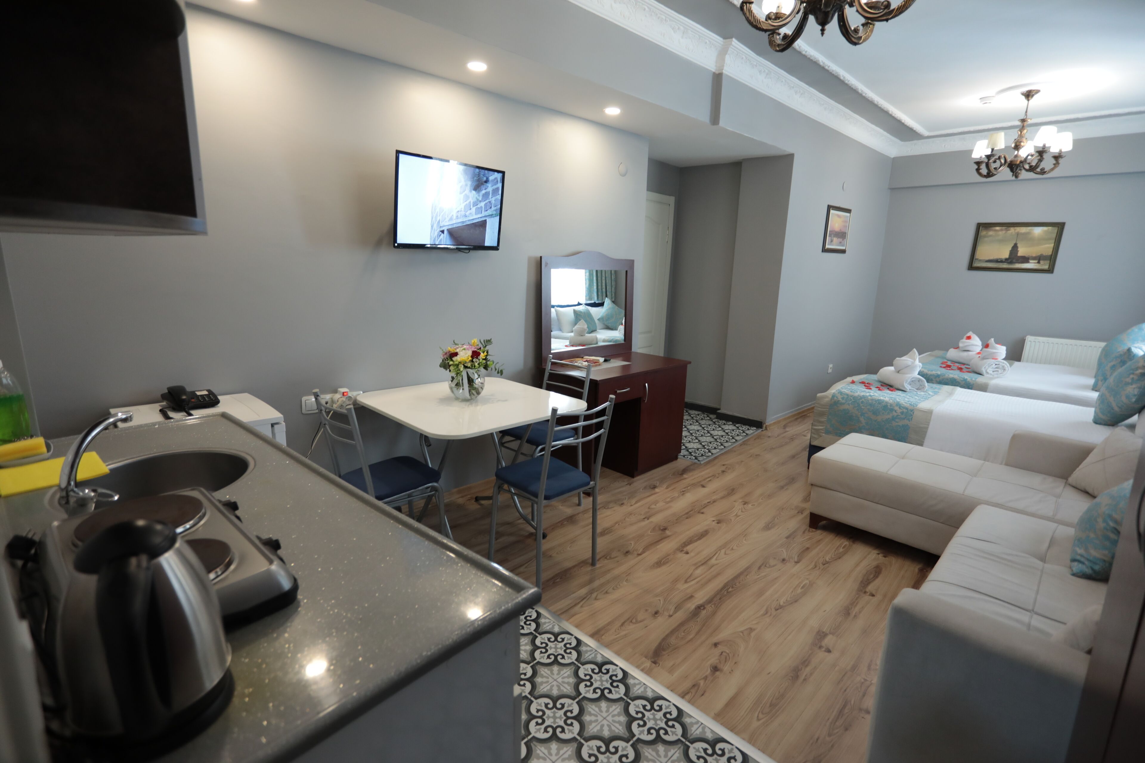 A modern kitchen with a kettle, a dining table with chairs, a small TV, and a sofa with cushions.