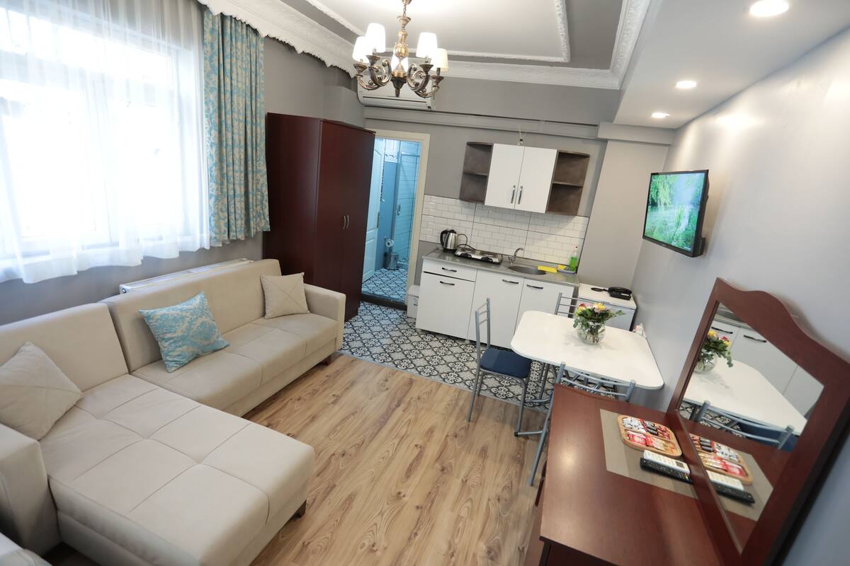 A modern living room with a sofa, a dining table, and a kitchen area with cabinets and a TV.