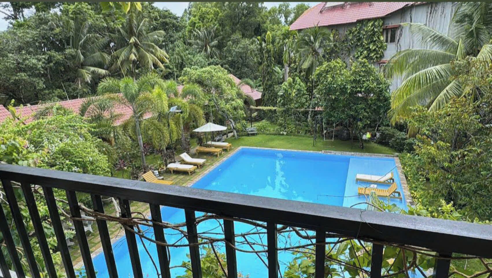 Piscina cercada por vegetação exuberante e um edifício com telhado vermelho.