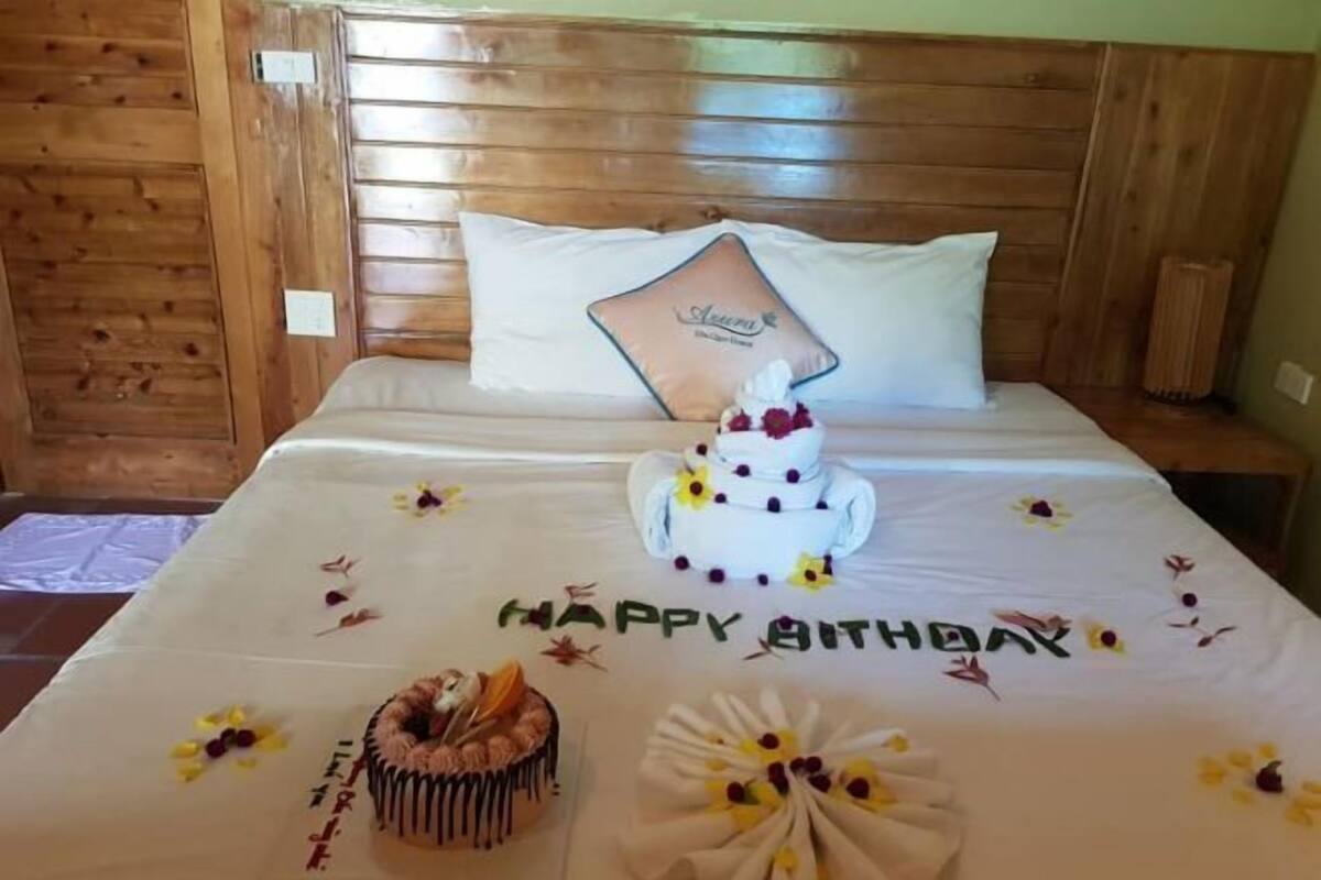 A bedroom with a wooden headboard, a bed with a white bedspread, a birthday cake, and a pillow with a logo.