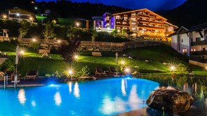A hotel with a swimming pool, outdoor seating, and a well-lit facade at night. - Jerzner Hof (Jerzens)