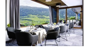 A restaurant with a table set for dining, a view of the countryside, and a wooden ceiling. - Jerzner Hof (Jerzens)