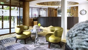 A reception area with a wooden ceiling, two green armchairs, a round table, and a reception desk. - Jerzner Hof (Jerzens)