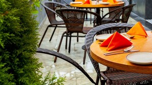 An outdoor patio with round tables, orange umbrellas, and wicker chairs. - Mango Suites Viera (Hyderabad)