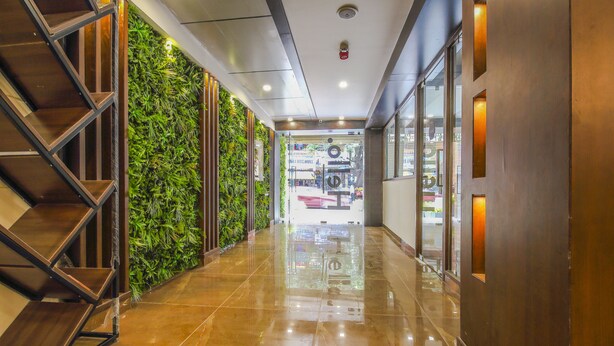 A hallway with a shiny tiled floor, a staircase on the left, and a wall with green plants. - Mango Suites Viera (Hyderabad)