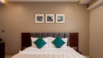 A hotel room with a large bed, two green pillows, a headboard, and three framed artworks on the wall.