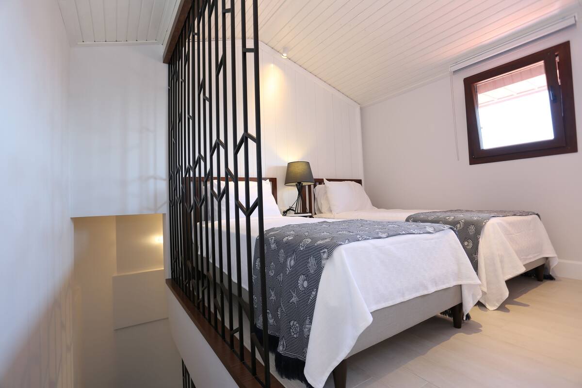 A bedroom with two beds, a window, and a nightstand with a lamp.