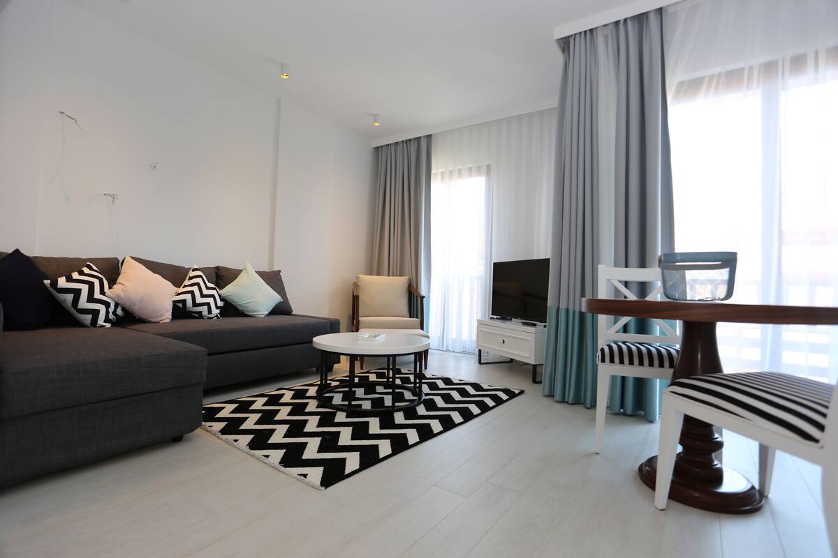 A modern living room with a grey sofa, a round coffee table, a white armchair, and a striped chair.