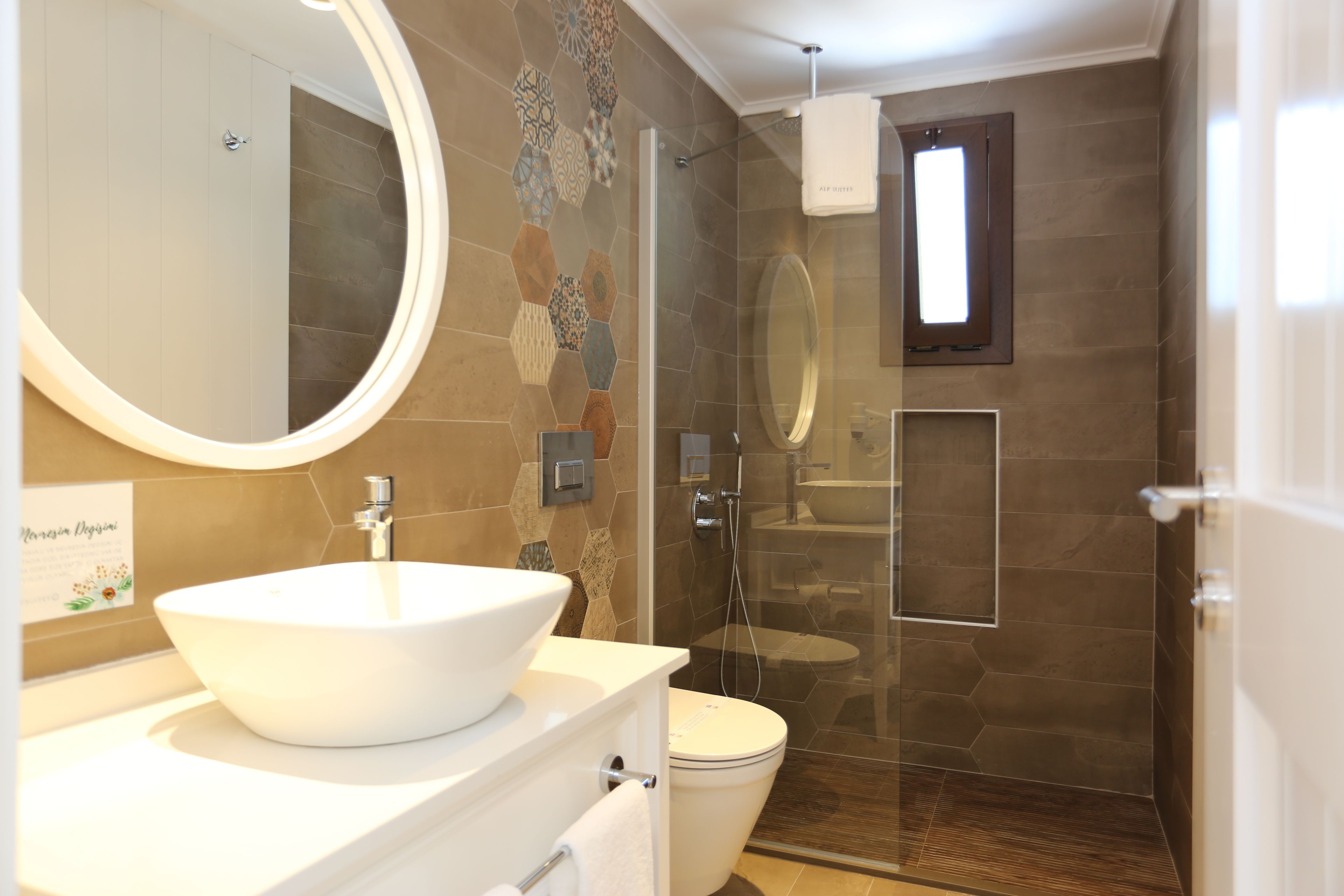 Un baño moderno con un espejo redondo grande, un lavabo blanco tipo recipiente y una zona de ducha con mampara de vidrio.
