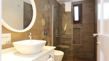 Un baño moderno con un espejo redondo grande, un lavabo blanco tipo recipiente y una zona de ducha con mampara de vidrio.