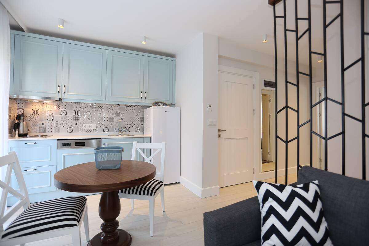 A modern kitchen with light blue cabinets, a white refrigerator, and a dining area with a round wooden table and striped chairs.