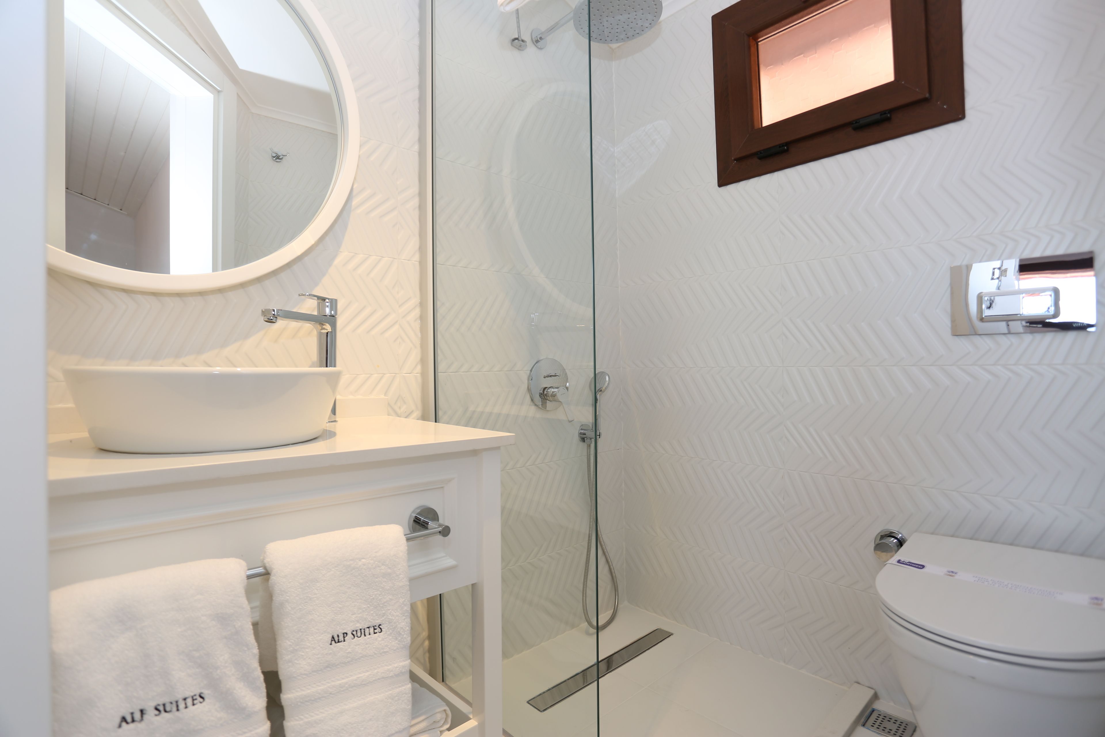 A modern bathroom with a round mirror, white sink, and a glass-enclosed shower.