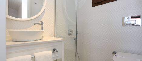 A modern bathroom with a round mirror, white sink, and a glass-enclosed shower.