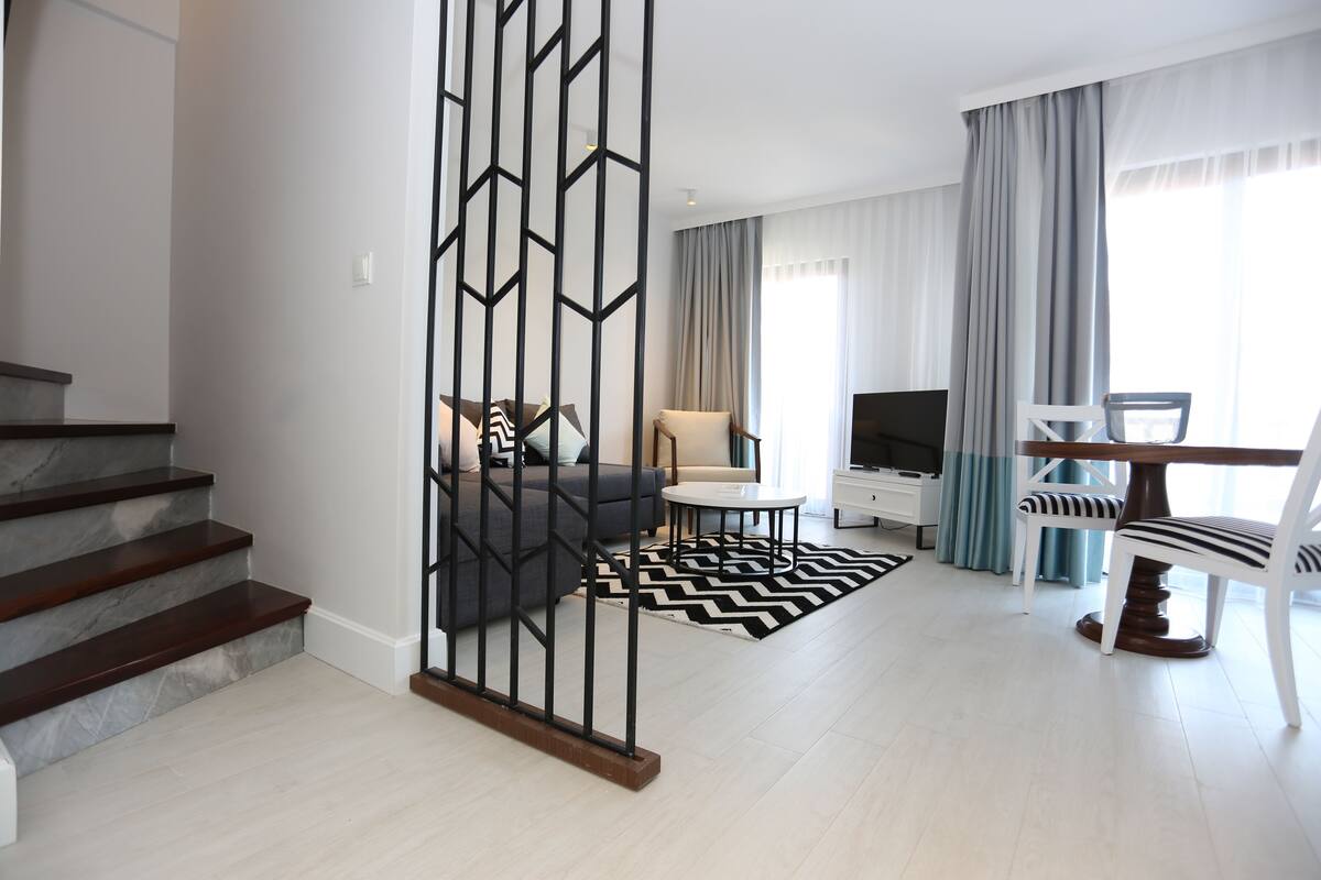 A modern living room with a staircase, a sofa, a TV, and a dining area.