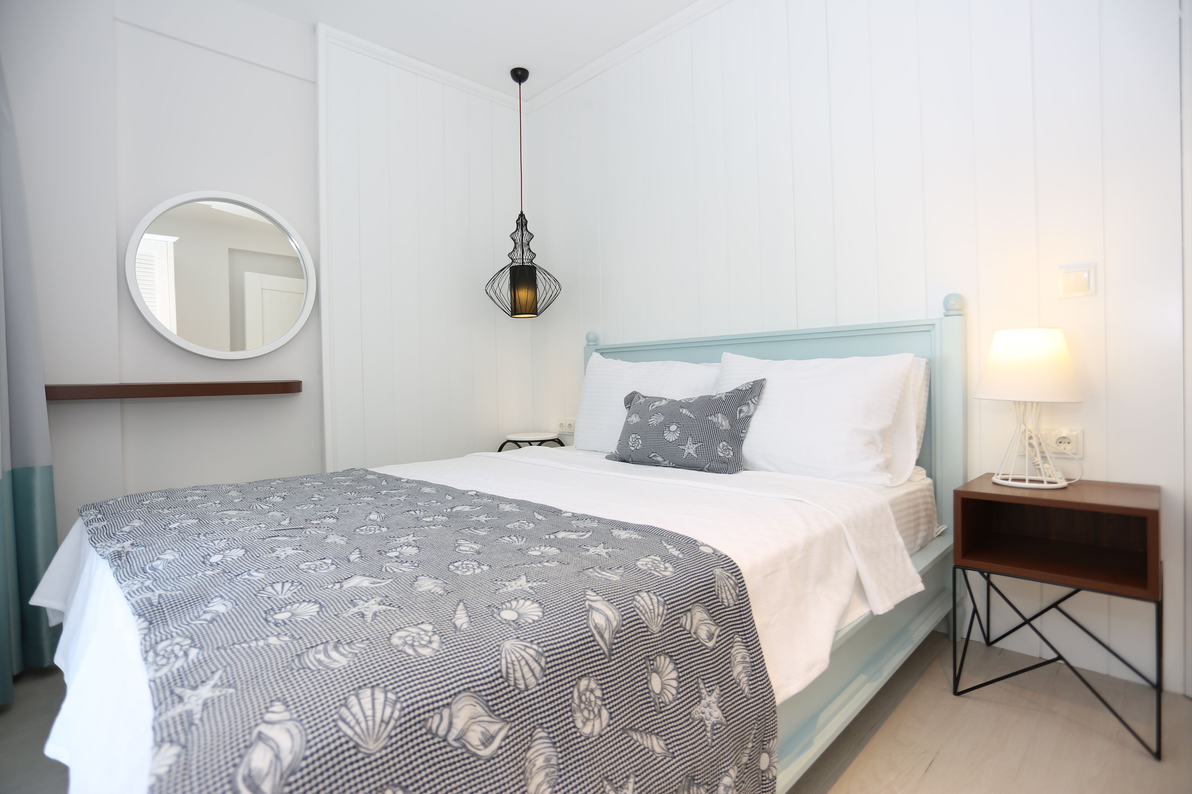 A neatly arranged bedroom with a bed, bedside table, lamp, and a hanging light fixture.
