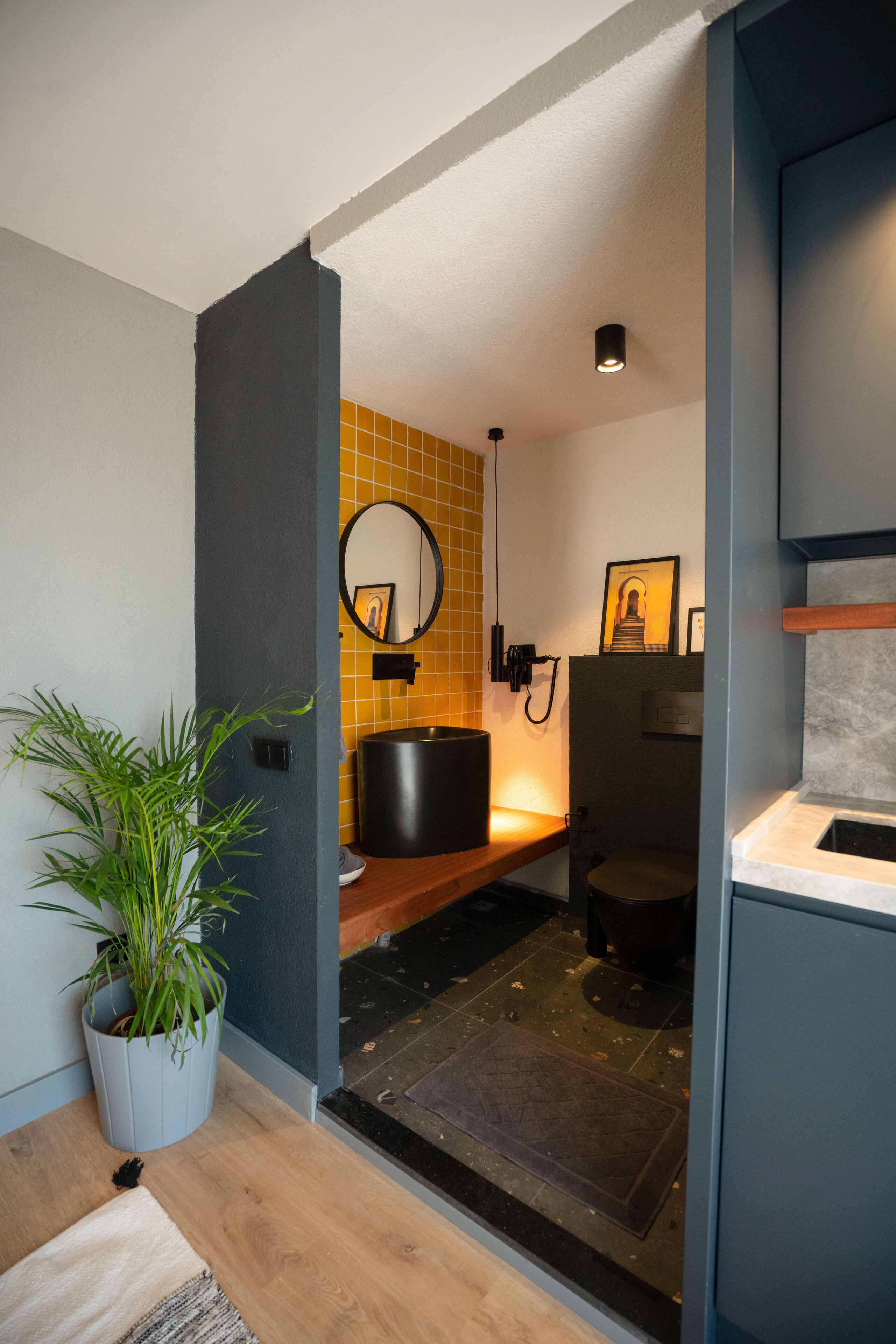 A modern bathroom with a wooden vanity, a sink, a mirror, and a potted plant.