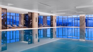 A modern indoor swimming pool with clear glass walls, lounge chairs, and a view of mountains. - Hangzhou Marriott Hotel Lin'an (Hangzhou)