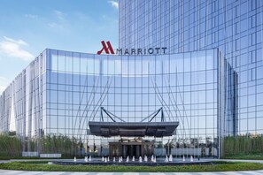A modern Marriott hotel with a glass facade, a prominent logo, and a fountain in front.