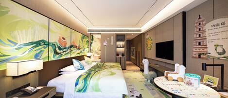 Habitación de hotel con una cama grande, un escritorio con computadora, televisión y una pared con obras de arte y un cartel.
