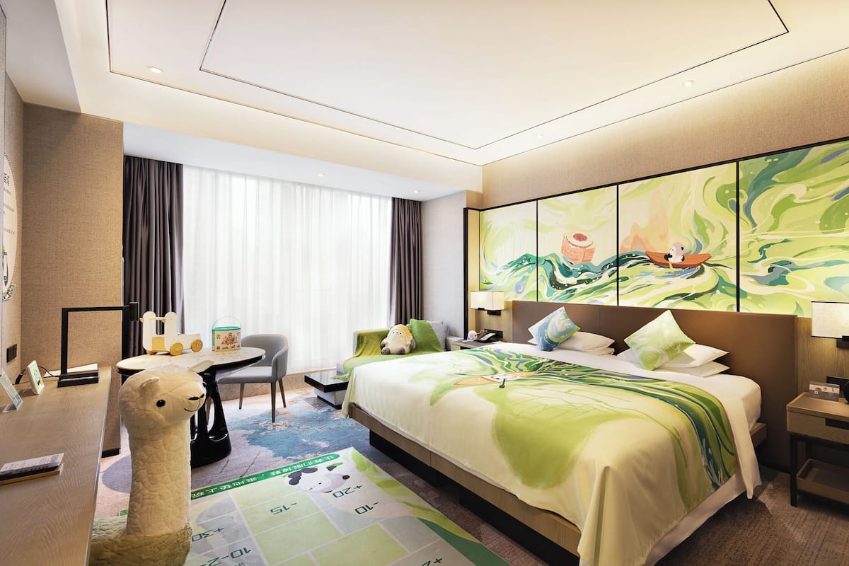 A hotel room with a bed, a desk, a chair, a TV, and a large window with curtains.